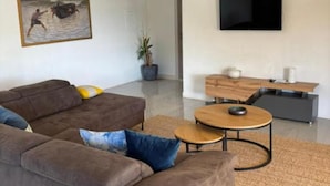 A modern living room with a brown sofa, a round coffee table, a flat-screen TV, and a painting of a man in water. - Villa Coral (Novo Selo)