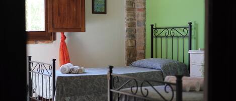 A room with a bed, a window with curtains, a painting on the wall, and a stone pillar.