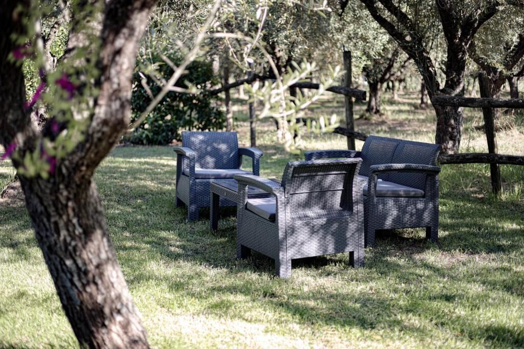 Arredamento da esterno in vimini in una zona erbosa, con alberi sullo sfondo.