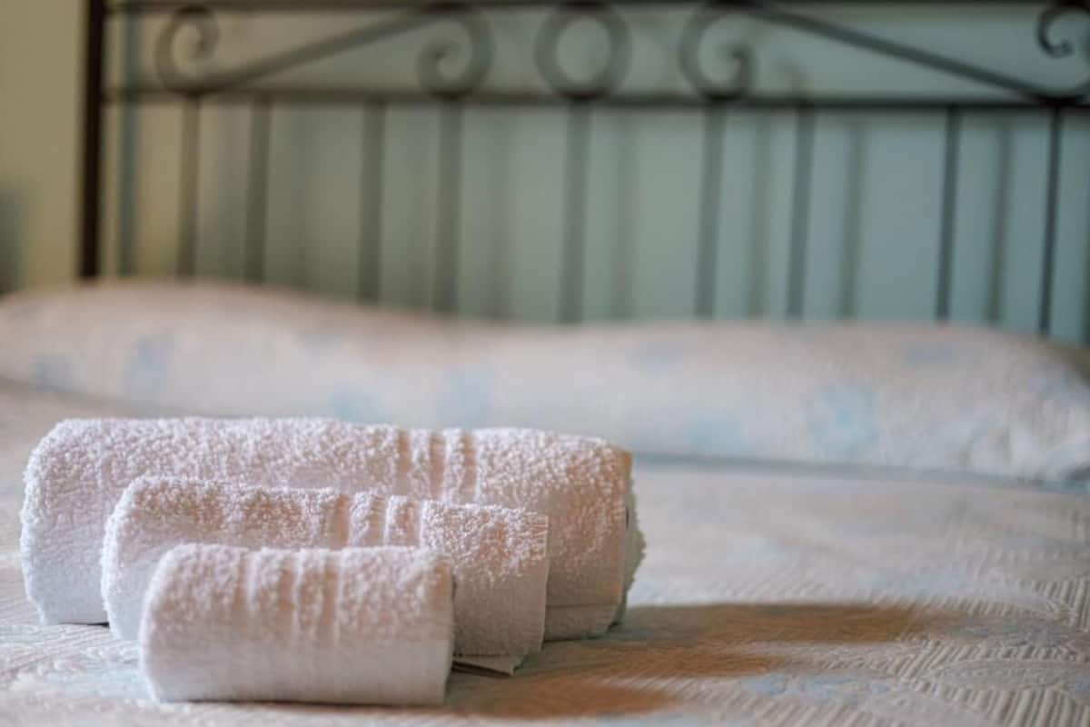 Un lit avec du linge de lit blanc et deux serviettes enroulées.