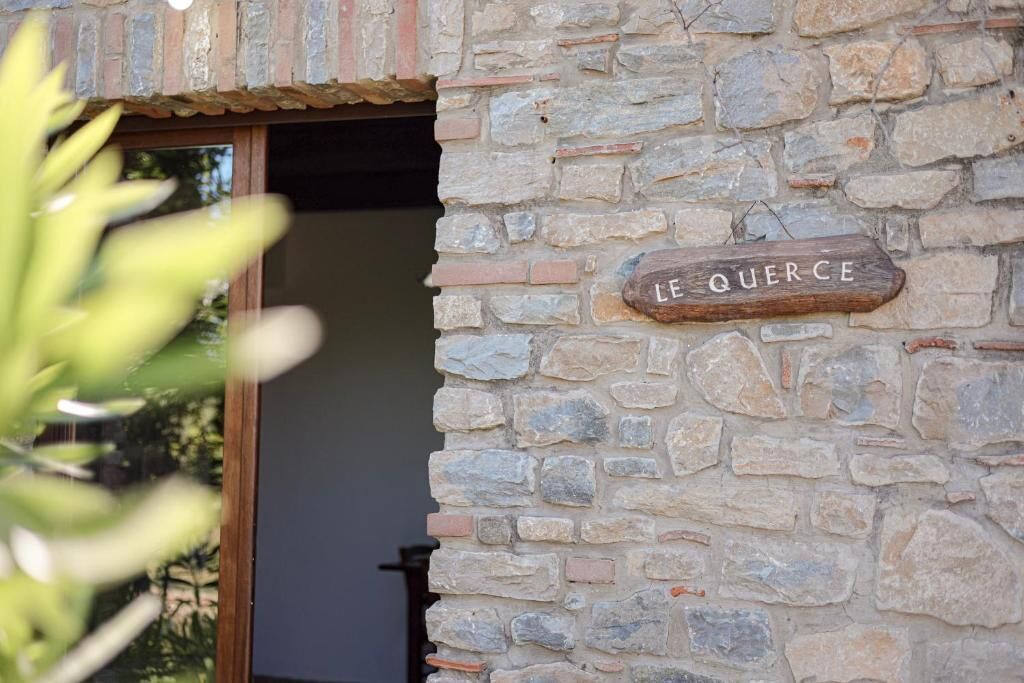 Un muro de piedra con un letrero de madera que dice 'LE QUERCHE'.