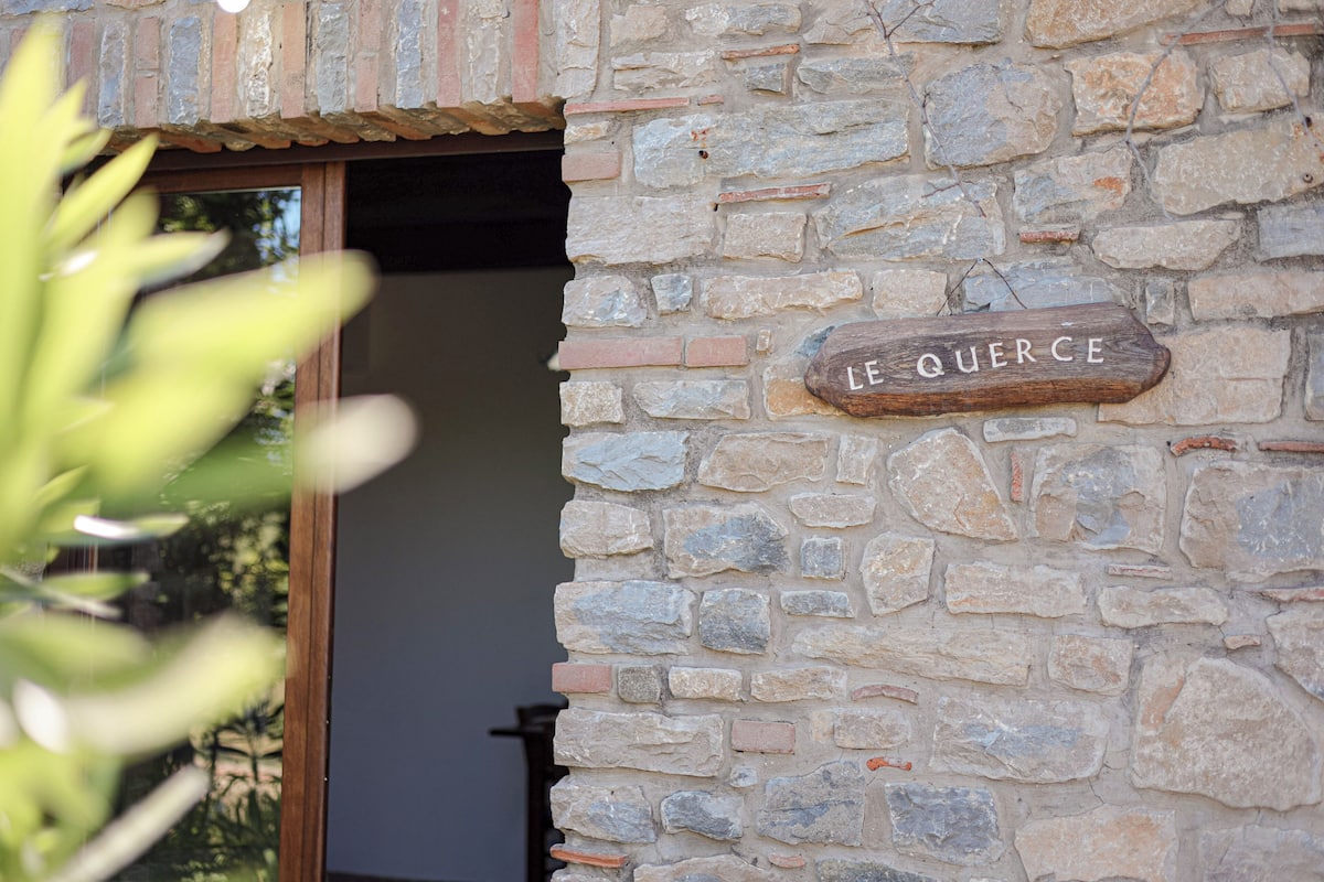 Un mur de pierres sur lequel est fixée une plaque en bois portant l’inscription « LE QUERCHE ».