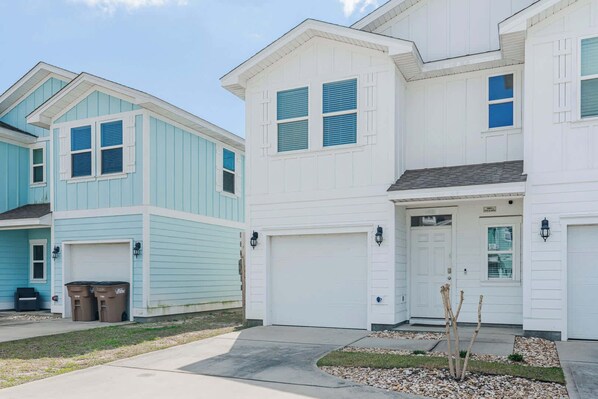 A residential area with two houses, one light blue and one white, with garage doors and a small garden. - Shadow Lake Retreat Quick Drive to Beach, Quiet Neighborhood (Panama City Beach)