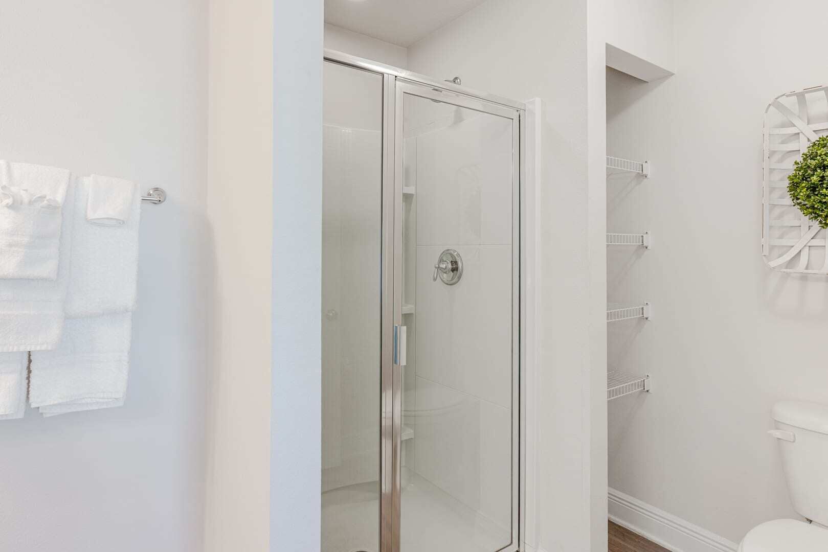 A bathroom with a glass shower door, white walls, and a toilet.