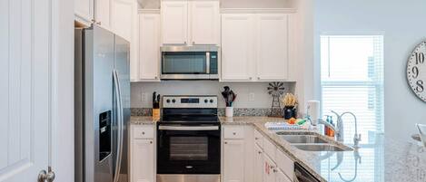 Una cocina moderna con armarios blancos, electrodomésticos de acero inoxidable, encimera de granito y un reloj en la pared.