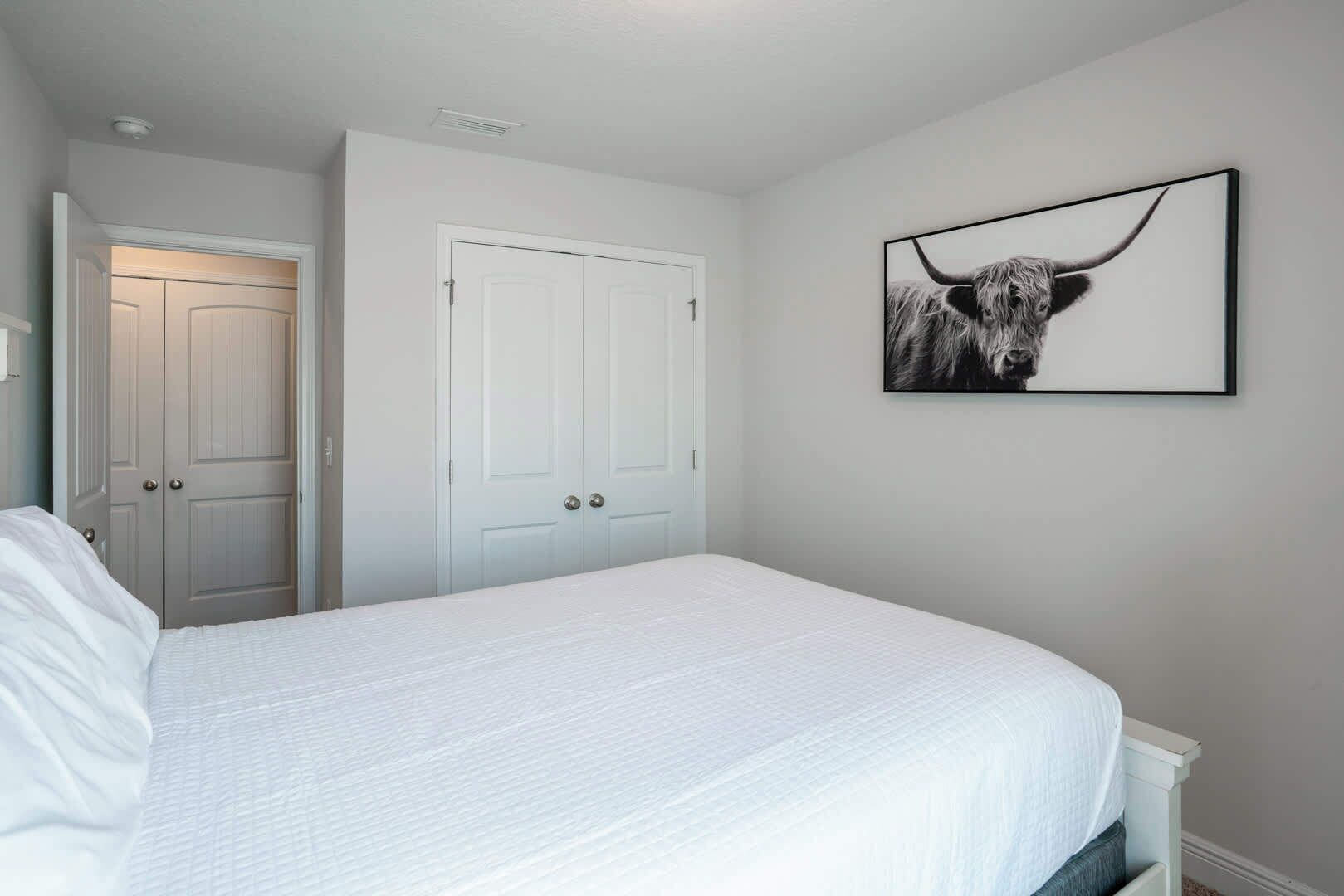 Un dormitorio con una cama, paredes blancas, una puerta y un cuadro con una imagen de toro.