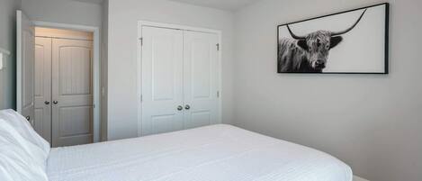Un dormitorio con una cama, paredes blancas, una puerta y un cuadro con una imagen de toro.
