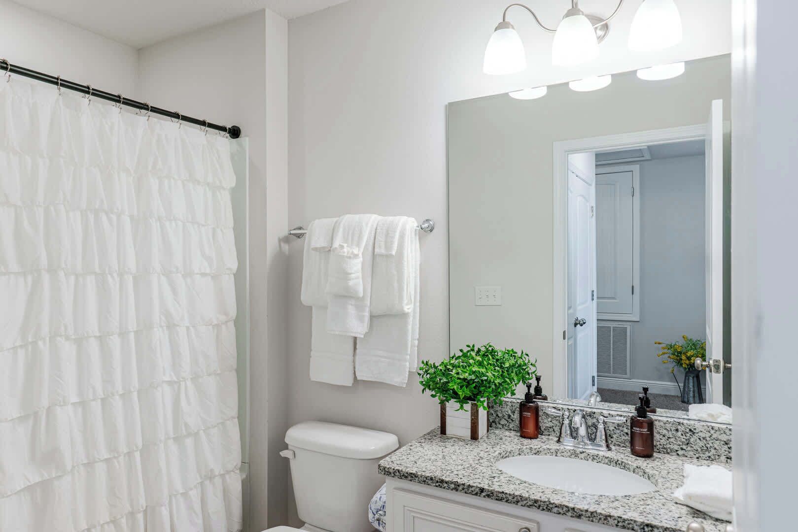 A bathroom with a shower curtain, a toilet, a sink with a mirror, and a potted plant.