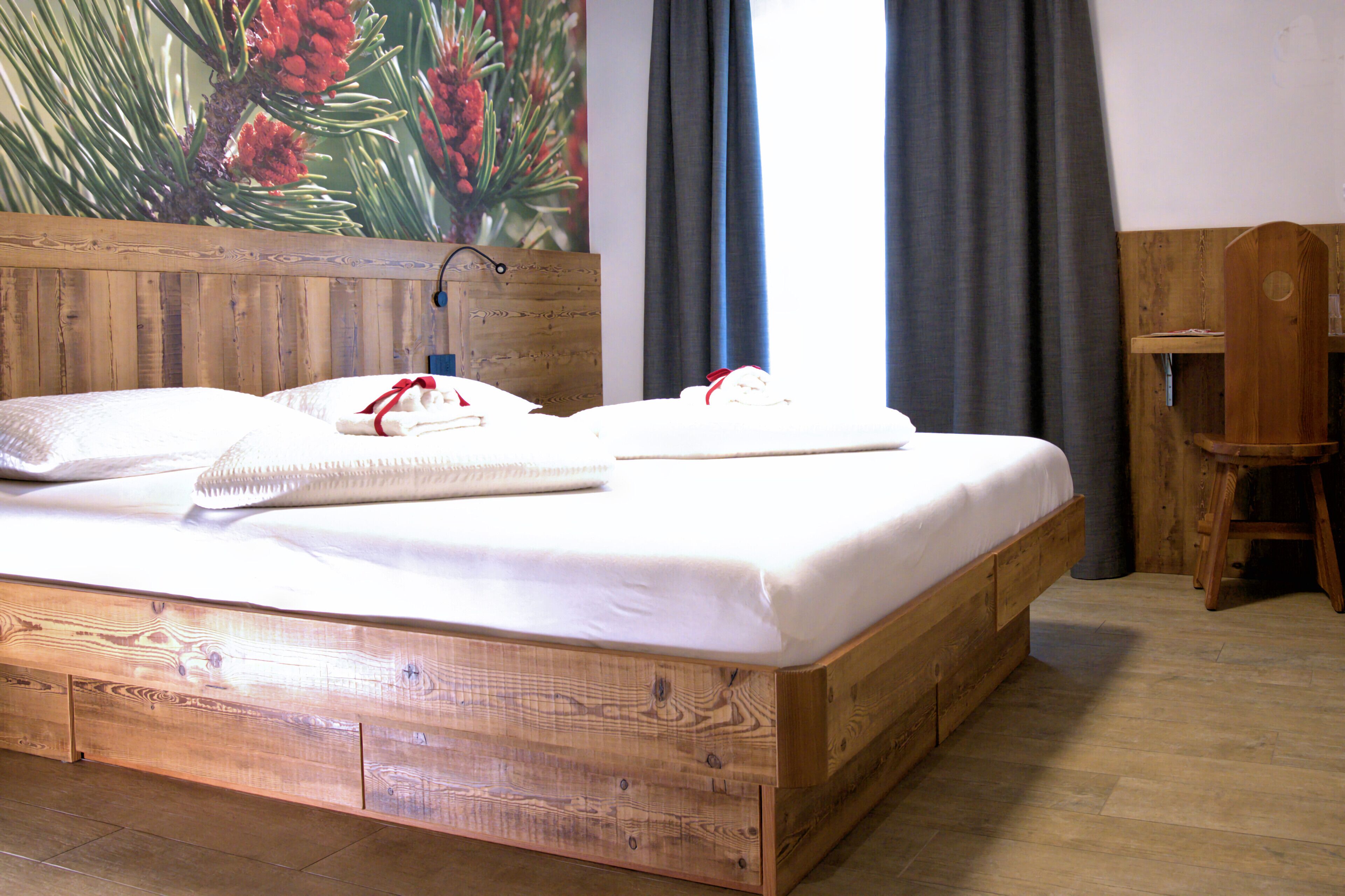 A wooden bed with white bedding, a wooden headboard, and a painting of pine cones.