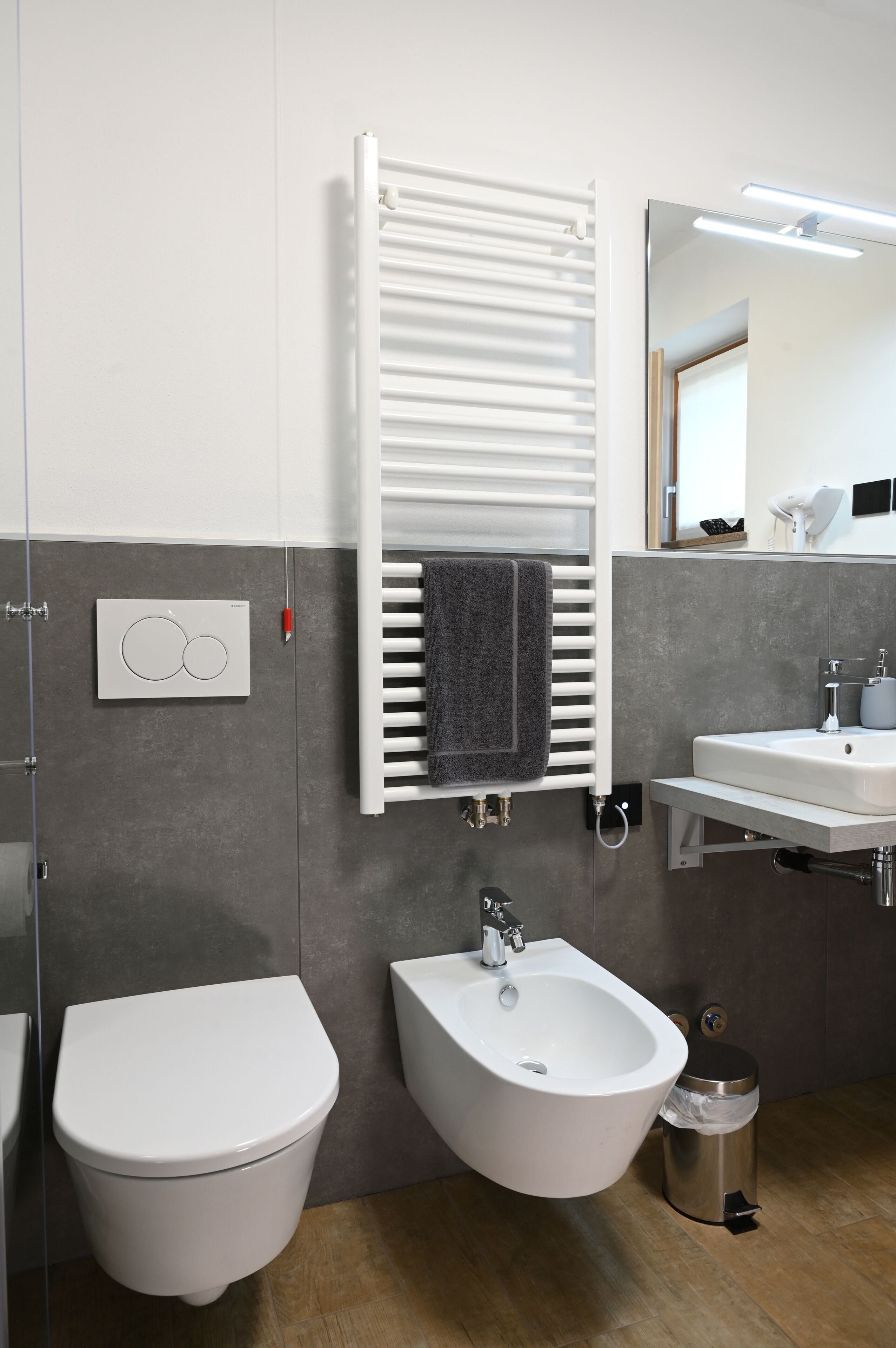 Un baño moderno con inodoro, bidé, lavamanos, toallero y espejo.
