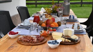 A wooden table set with various food items, including fruits, cheeses, and meats, outdoors with a fence and greenery in the background. - Mas dei Masi (Cavalese)
