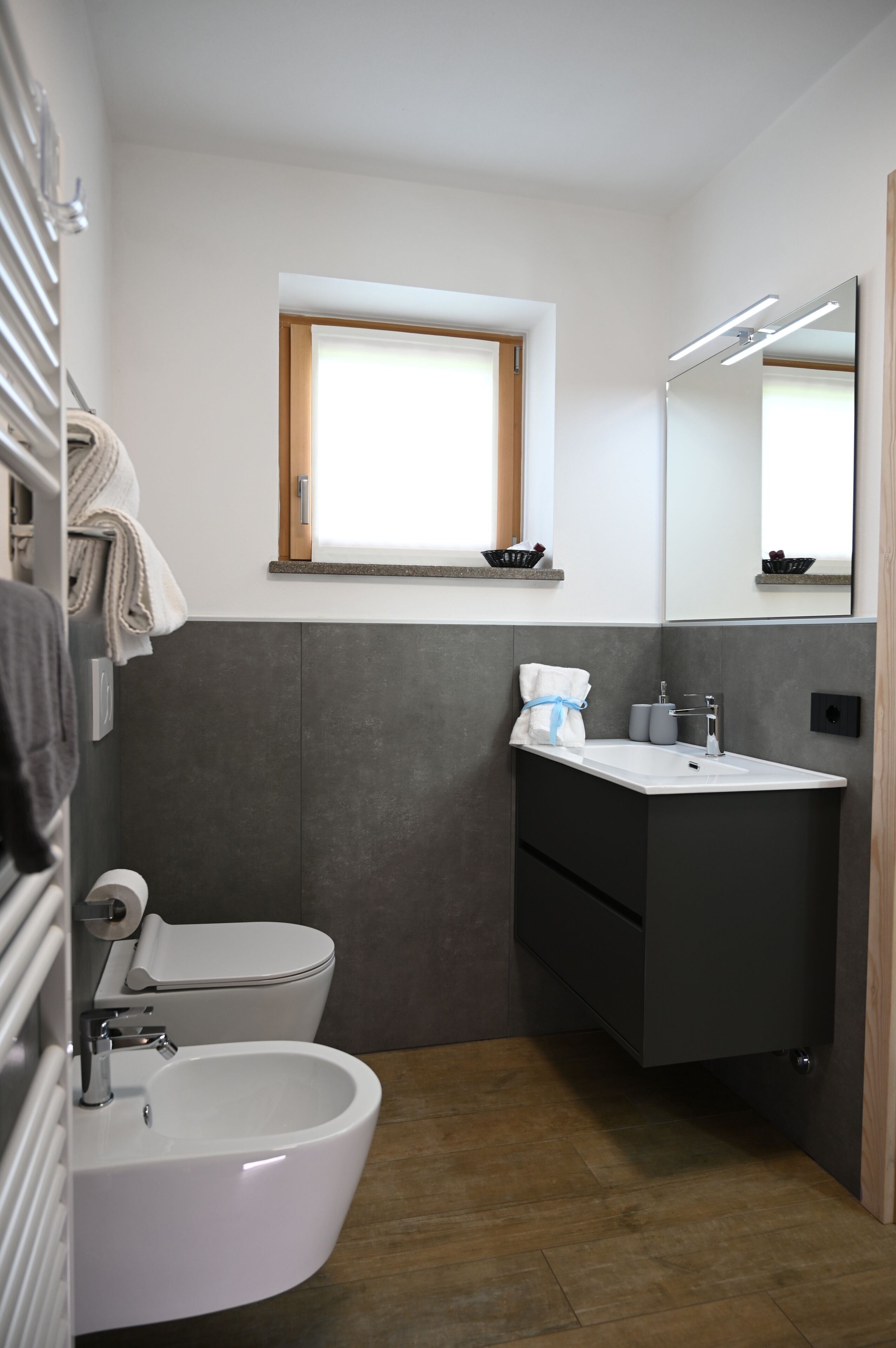 Et lille badeværelse med toilet, bidet, vask og spejl.