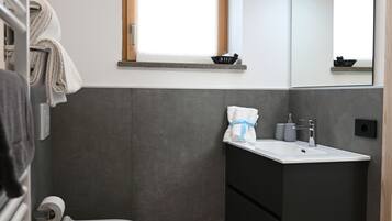 Et lille badeværelse med toilet, bidet, vask og spejl.