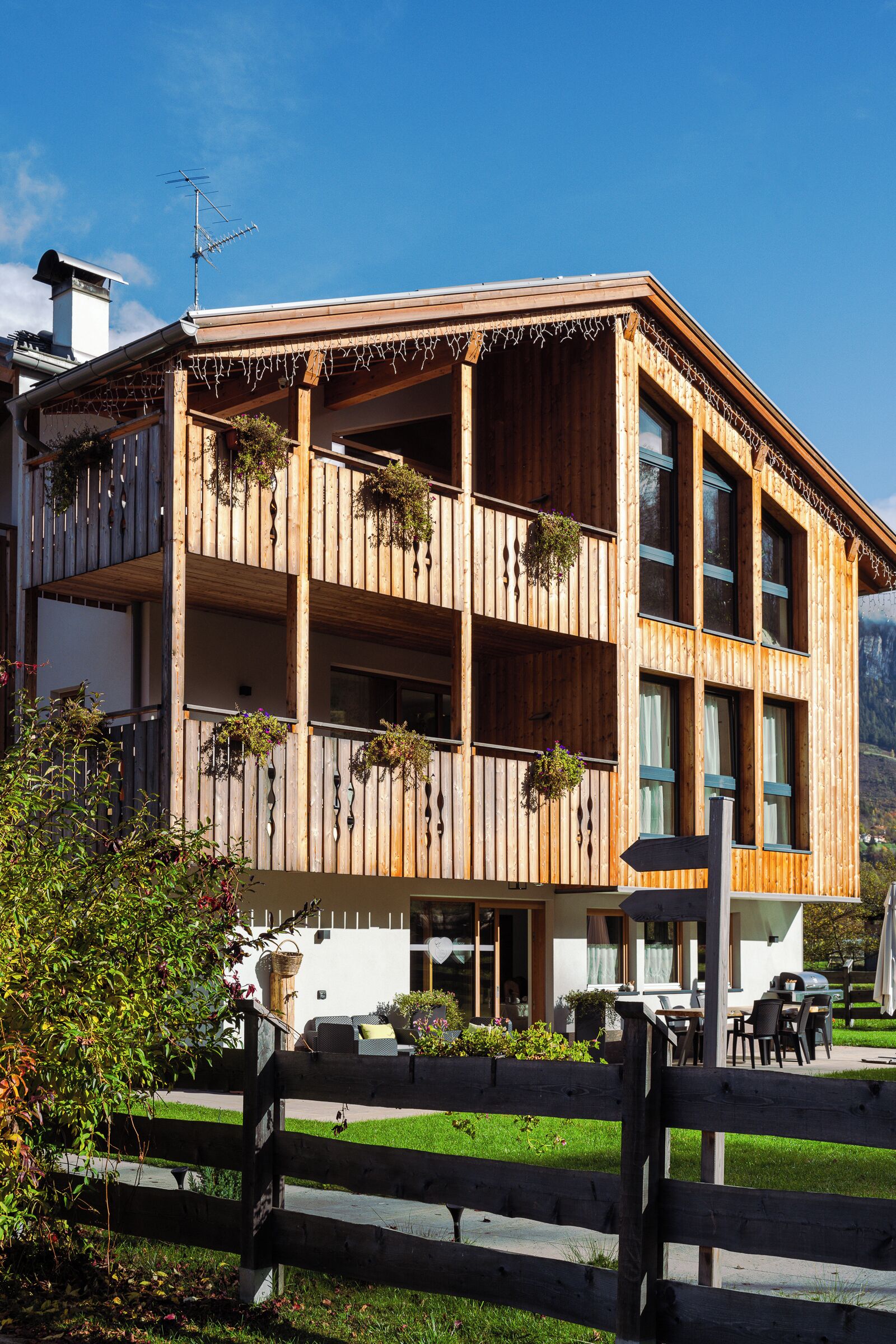 Un edificio de madera de varios pisos con balcones, una chimenea visible y un pequeño espacio al aire libre para sentarse.