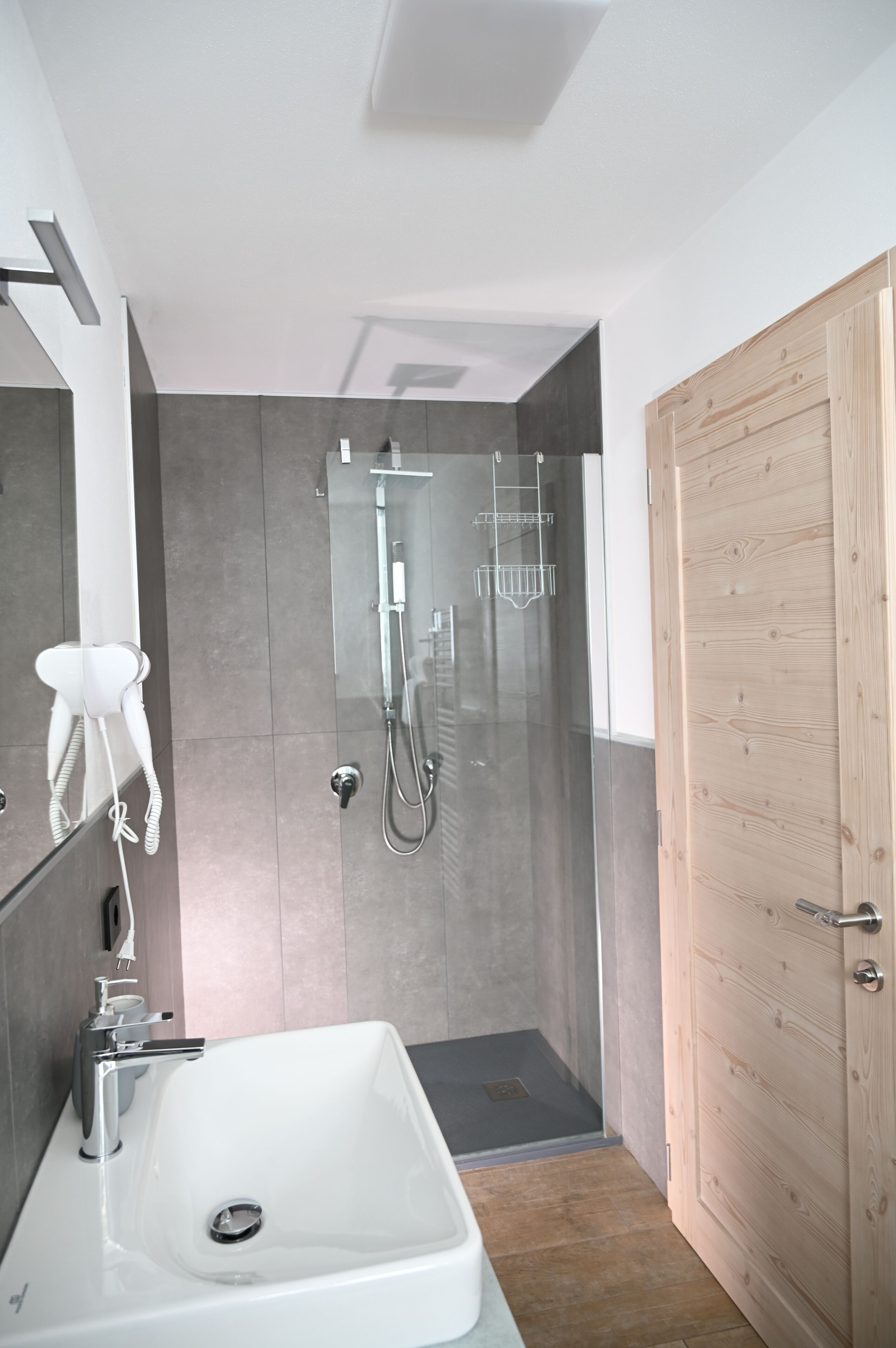 A modern bathroom with a glass-enclosed shower, a white sink, and a wooden door.
