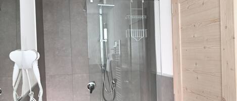 A modern bathroom with a glass-enclosed shower, a white sink, and a wooden door.