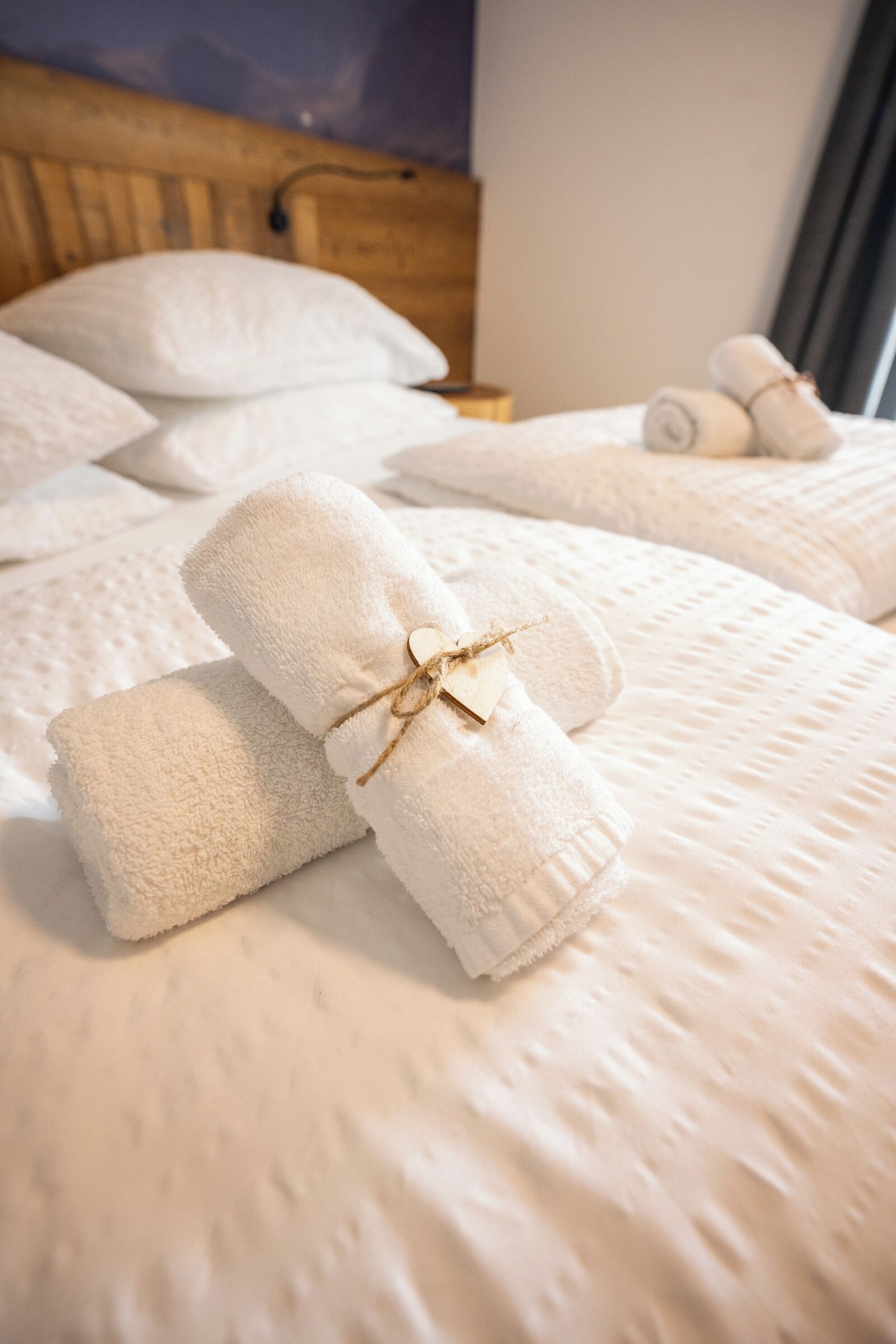 Ein ordentlich bezogenes Bett mit aufgerollten weißen Handtüchern und einem Holzkopfstück.