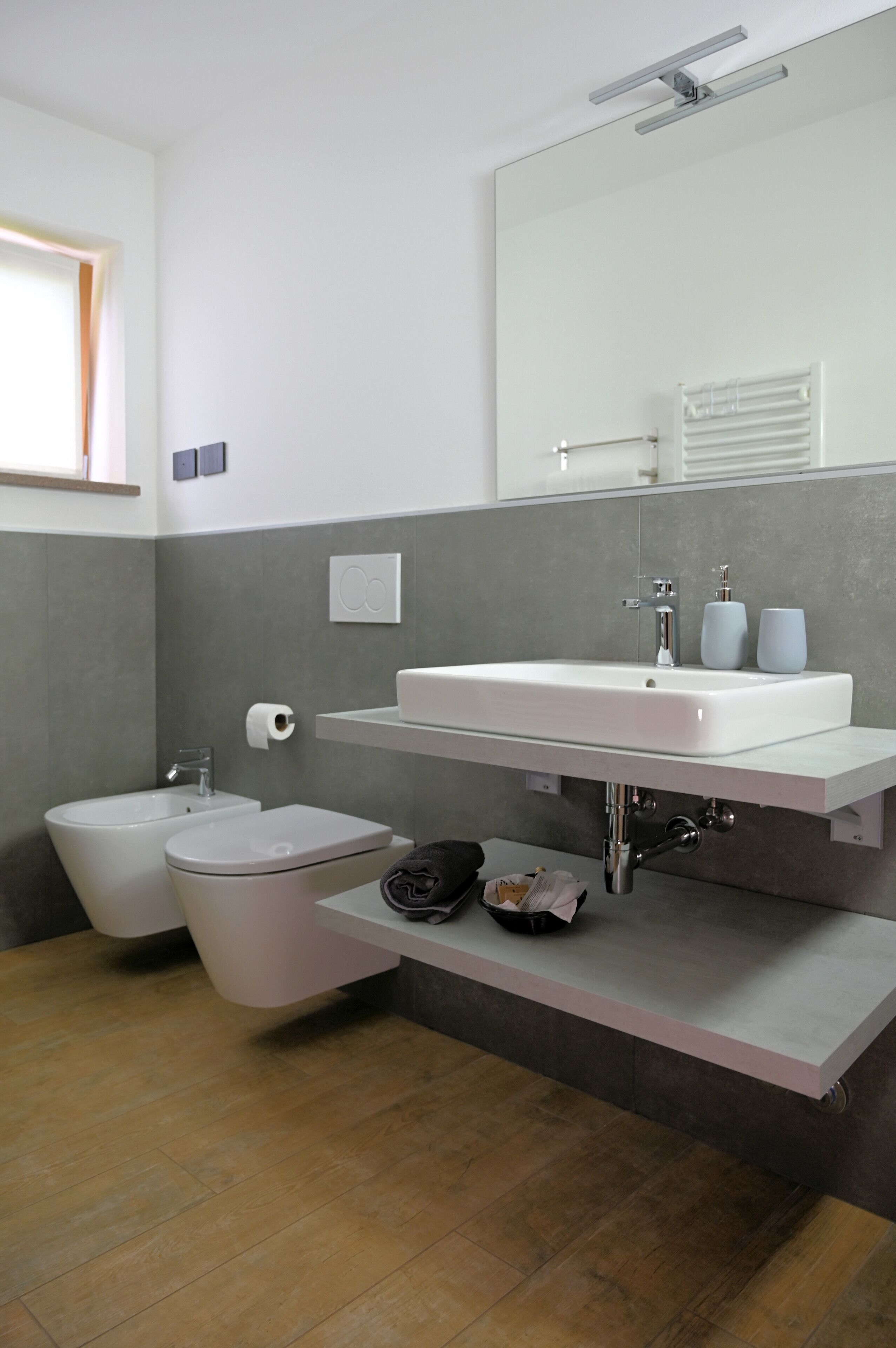 A modern bathroom with a bidet, toilet, and a large mirror above a white sink.