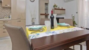 A dining area with a table set for two, a wine bottle, and a clock on the wall. - Apartment Kancijanić (Vodnjan)