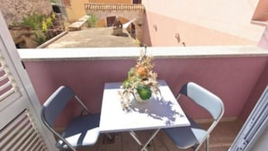 A balcony with a table and two chairs, a potted plant, and a view of a building in the background. - Apartment Kancijanić (Vodnjan)