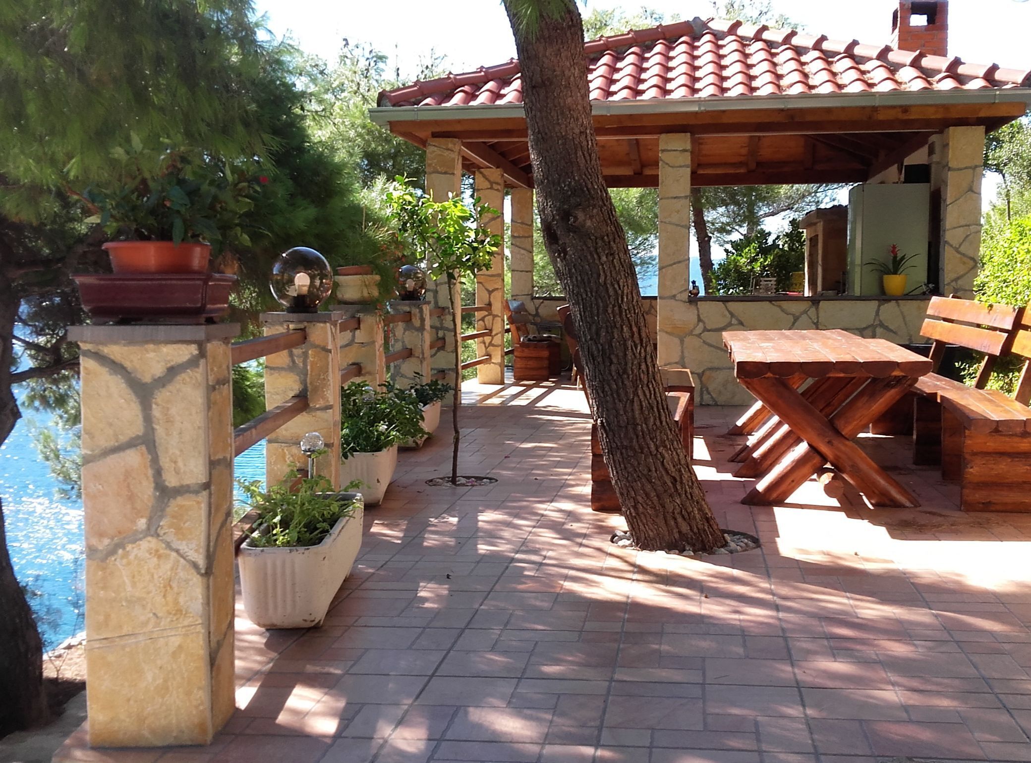 Un patio al aire libre con pilares de piedra, bancos de madera y plantas en macetas.