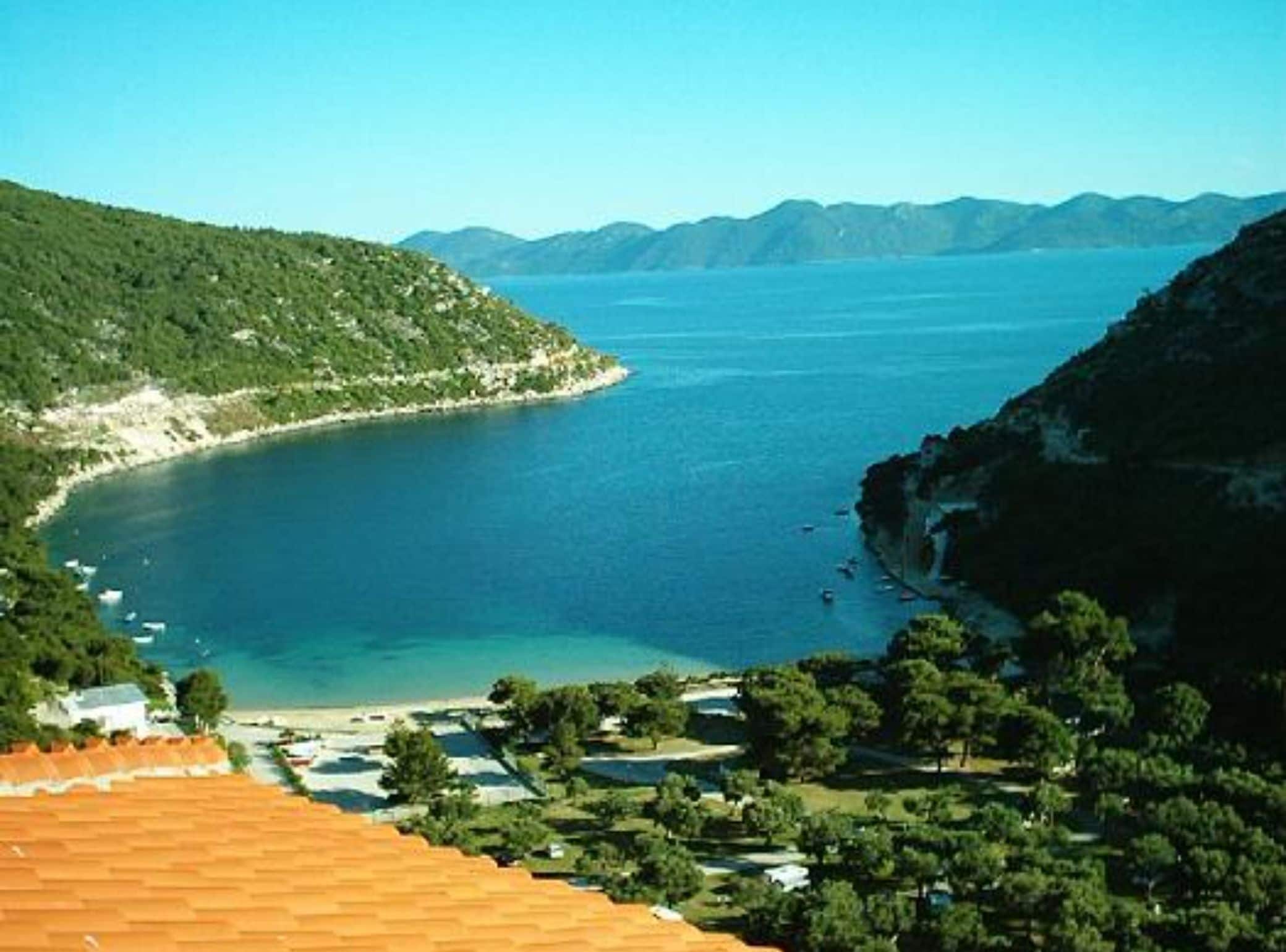 A coastal landscape with a clear view of the sea, a beach, and a mountainous backdrop.