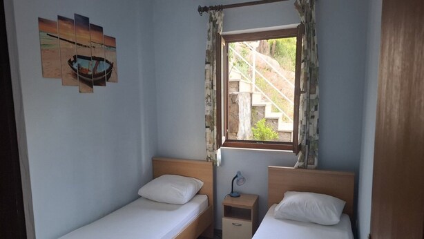 Une petite chambre avec deux lits simples, une table de chevet avec une lampe et une fenêtre avec des rideaux.