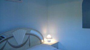 A hotel room with a bed, a nightstand with a lamp, a framed picture on the wall, and a window with a view. - Josip Blue Horizon Apartments (Ston)