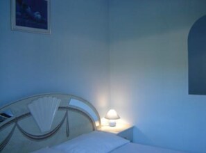 Ein Hotelzimmer mit einem Bett, einem Nachttisch mit Lampe, einem gerahmten Bild an der Wand und einem Fenster mit Aussicht.