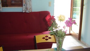 Un canapé rouge, un vase en verre avec des fleurs et une fenêtre avec des rideaux.