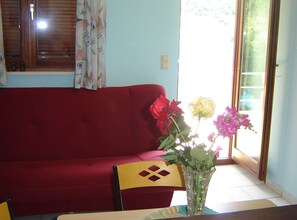 Ein rotes Sofa, eine Glasvase mit Blumen und ein Fenster mit Vorhängen.