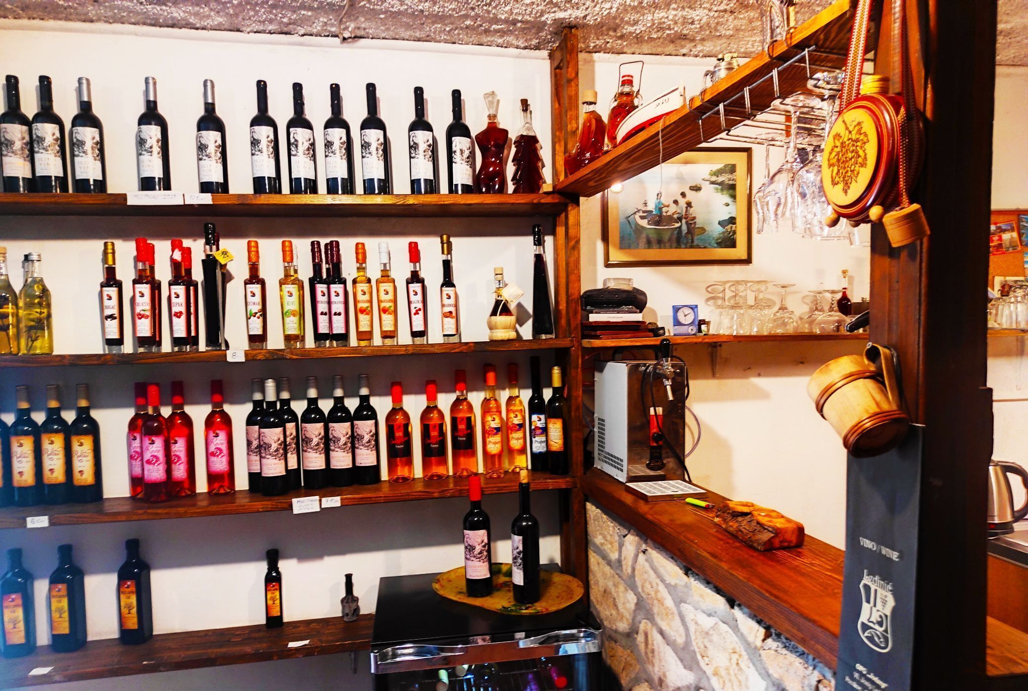 A wine cellar with shelves of wine bottles, a wooden counter, and a stone wall.