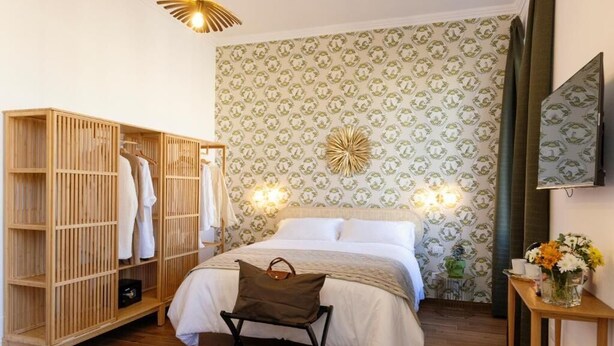 A bedroom with a bed, wooden wardrobe, and a bedside table with a vase of flowers. - Risorgimento 55 (Rome)