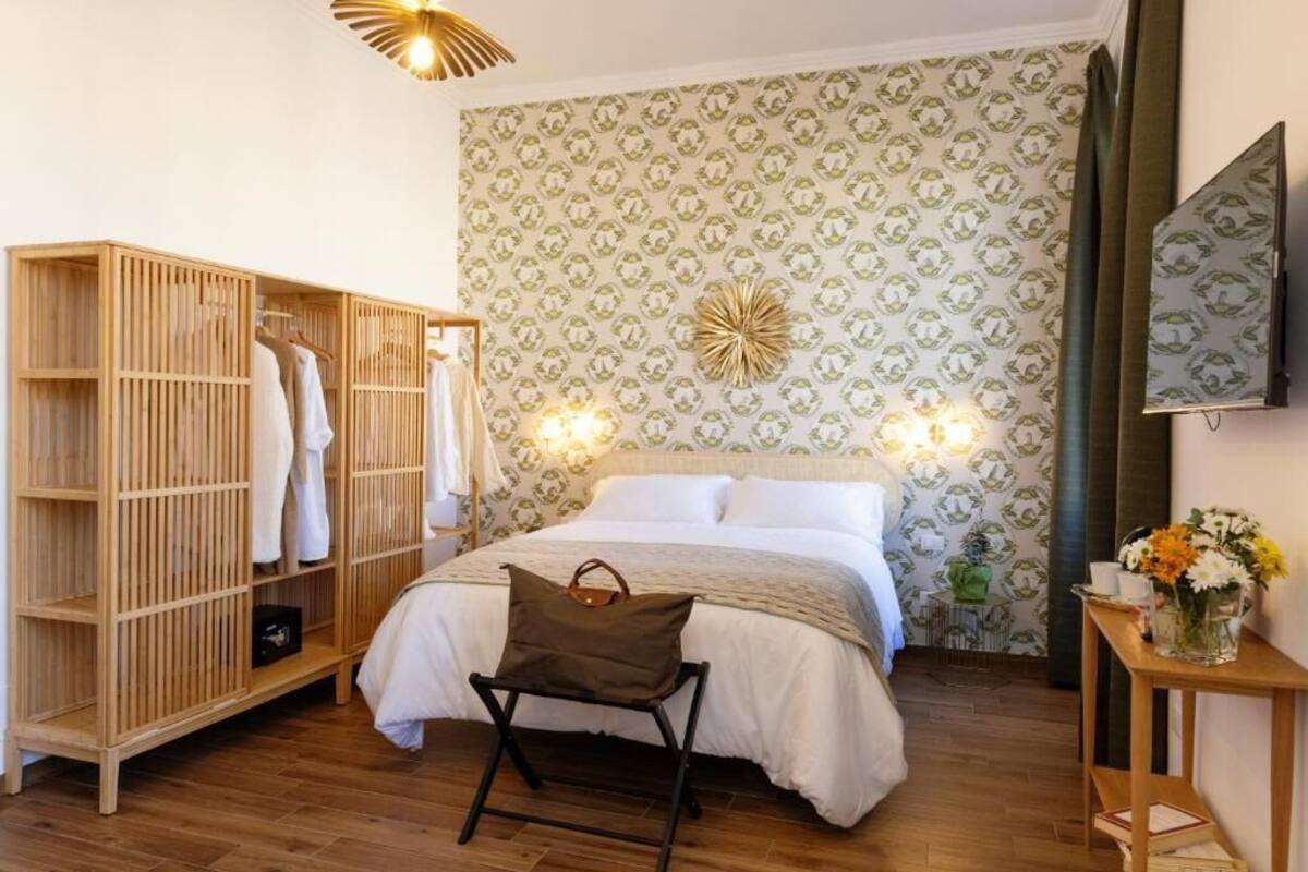 A bedroom with a bed, wooden wardrobe, and a bedside table with a vase of flowers.