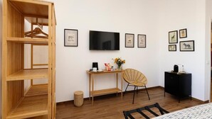 A room with a wooden wardrobe, a TV, a wicker chair, a small table with a vase and a coffee machine, and framed pictures on the wall. - Risorgimento 55 (Rome)