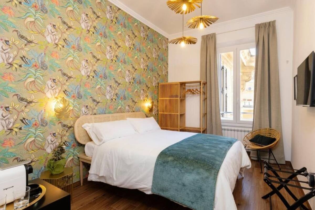 A bedroom with a bed, a bedside table, a chair, a wardrobe, and a window with curtains.