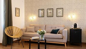 A living room with a sofa, a wicker chair, a small table with a book and flowers, and a black cabinet. - Risorgimento 55 (Rome)