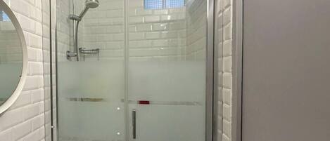 A glass-enclosed shower with a handheld showerhead, a glass door, and a white tiled wall.