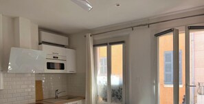 Eine moderne Küche mit Mikrowelle, Backofen und Spüle. Eine Schiebetür aus Glas führt in einen Außenbereich mit Blick auf ein Gebäude mit blauen Fensterläden.