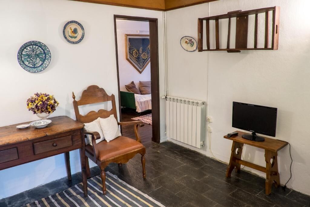 Una stanza con una sedia in legno, una scrivania con un vaso di fiori, un televisore su un mobile e piatti decorativi appesi al muro.