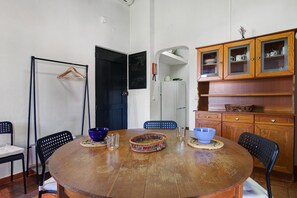 Una mesa de comedor redonda de madera con sillas, un perchero, un refrigerador blanco y armarios de madera con puertas de vidrio.