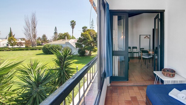 A balcony with a view of a well-maintained lawn and trees, a bed with a blue cover, and a table with a basket. - Pedras del Rei 8 (Pedrinhas del Rei) (Santa Luzia)