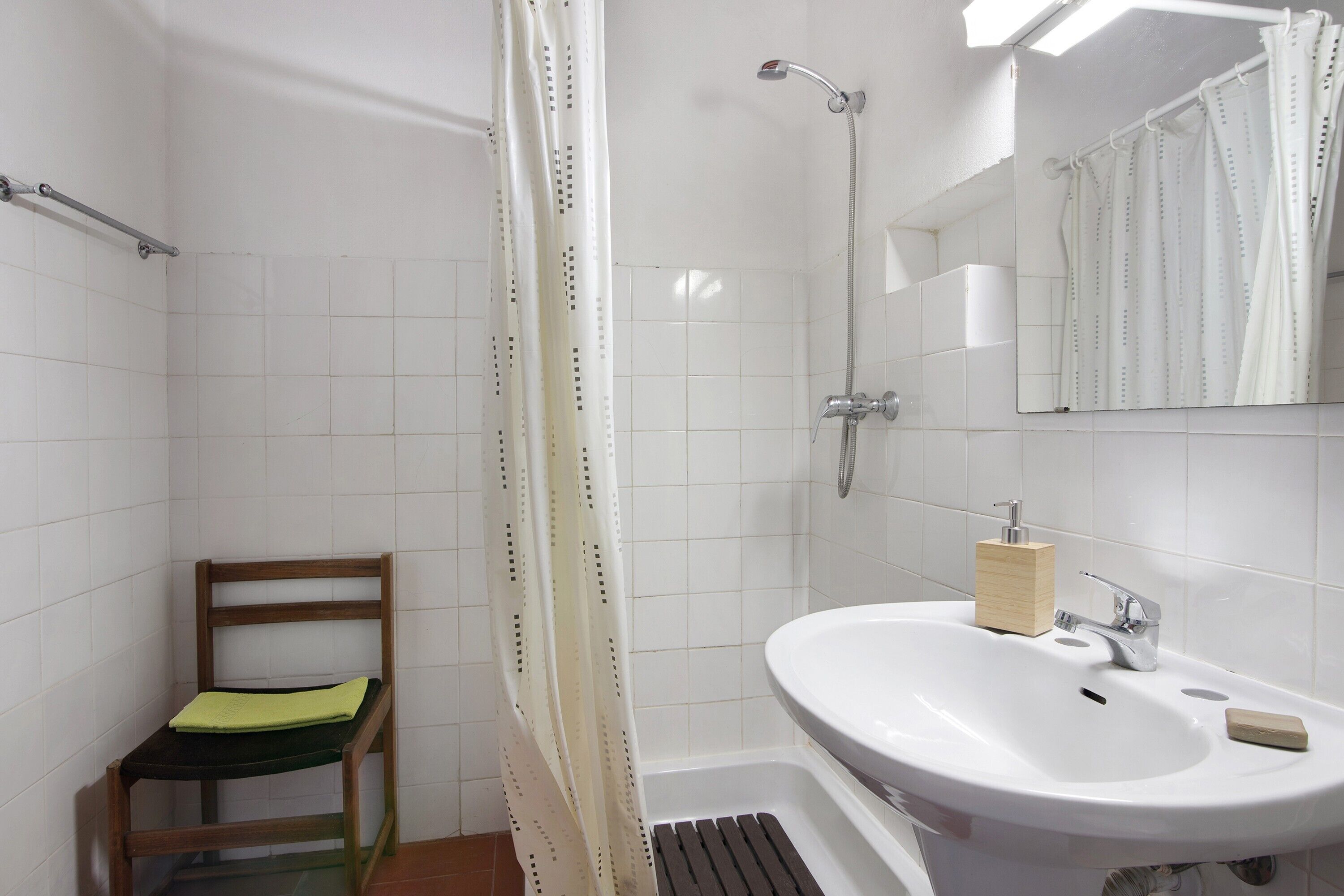 A bathroom with a shower, a sink, a mirror, and a wooden chair.