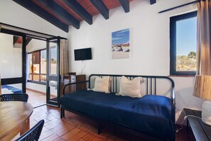 Una habitación con cama, televisión, mesa y ventana con cortinas.