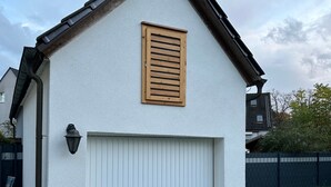 Un bâtiment blanc avec une porte de garage, un volet en bois et une petite fenêtre.