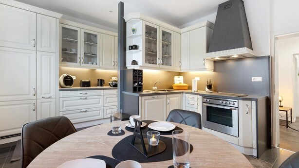 Une cuisine moderne avec des meubles blancs, un îlot central et un four encastré.