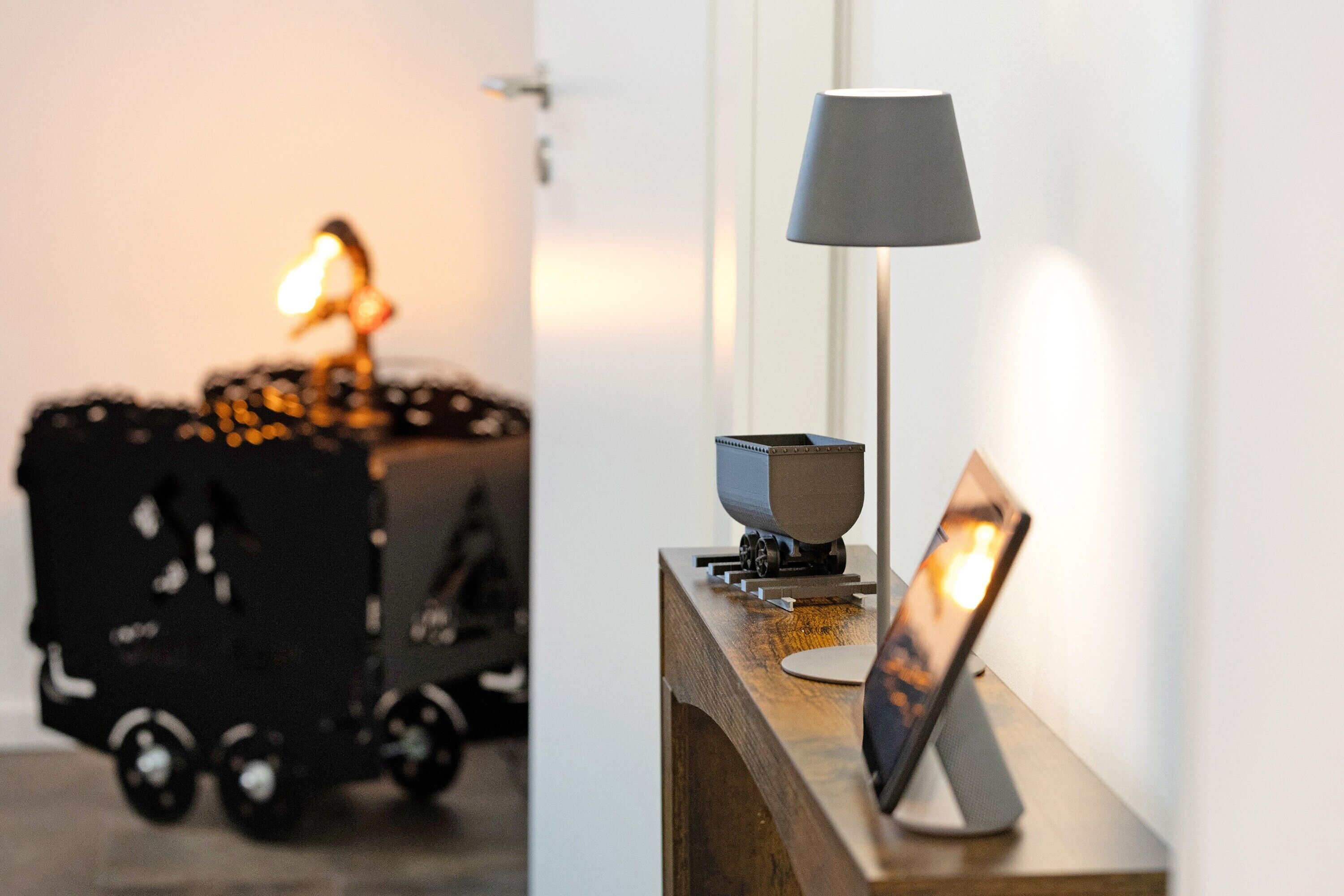 Une pièce avec un bureau en bois, une lampe, un petit modèle de bateau et une poussette.