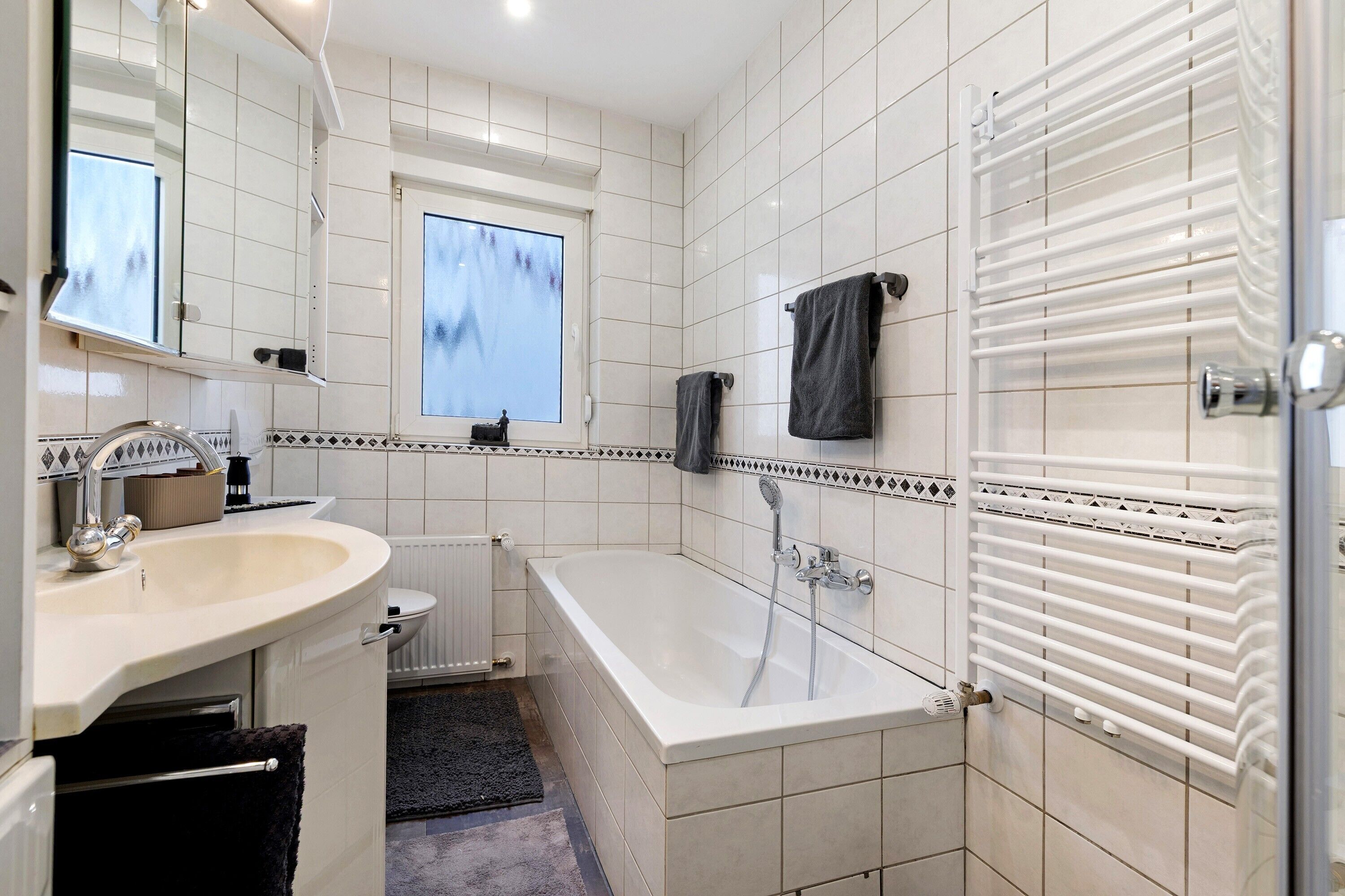 A bathroom with a bathtub, a sink, a mirror, and a window.