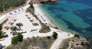 A coastal hotel with outdoor seating, a beach, and a rocky shoreline.