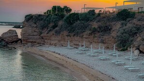 Ein Strand mit weißen Sonnenschirmen und einer felsigen Klippe.